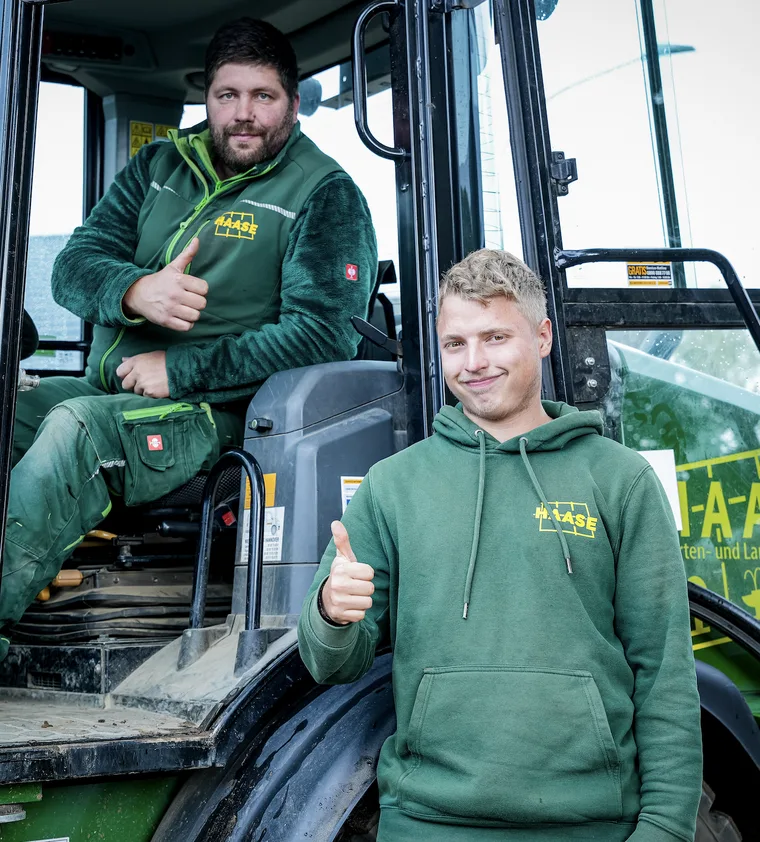 Zwei Mitarbeiter der Firma Haase zeigen vor einem Traktor den Daumen nach oben